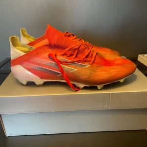 Adidas - fotbollsskor i röd och vit färg med silverdetaljer. Skorna har snörning och är designade för maximal fart och grepp på planen. Perfekta för dig som vill ta ditt spel till nästa nivå.