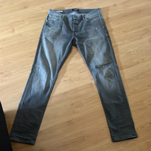 Jack and Jones jeans, slim/glenn - Säljer ett par grå jeansbyxor från Jack and Jones. Byxorna har diskreta slitningar framtill och stängs med dragkedja och knapp. Perfekta för en avslappnad stil.