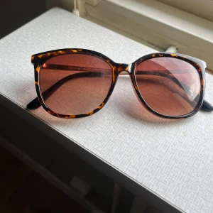 Bruna solglasögon med leopardmönster - Snygga solglasögon med brunt leopardmönstrat båge och stora, lätt cat-eye formade glas. Glasen är tonade i brunt och bågarna är i plast. Perfekt accessoar för att lyfta din stil.