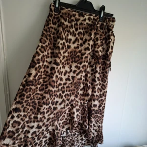 Leopardmönstrad omlottkjol med volang - Säljer en snygg leopardmönstrad omlottkjol med volangdetaljer. Kjolen har en längre modell och knyts i midjan. Perfekt för dig som vill sticka ut med ett djurmönster och gillar flowiga kjolar.