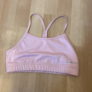 Ljusrosa sport-bh från stadium - Säljer en ljusrosa sport-bh från stadium med smala axelband och enkel design. Perfekt för träning och aktiviteter där du vill ha något bekvämt och stilrent. Materialet är mjukt och stretchigt.