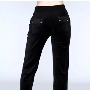 Svarta Juicy Couture  - Svarta mjukisbyxor med bred resår i midjan och snörning framtill. Byxorna har fickor både fram och bak med lock och knappdetaljer. Mjukt material som ger en avslappnad look.