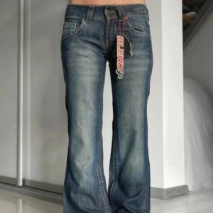 Blå bootcut jeans från Blend - Säljer ett par klassiska blå bootcut jeans från Blend med snygga slitningar och femficksmodell. Jeansen har låg midja och en något utsvängd passform nertill. Perfekta för dig som gillar retrostilen!