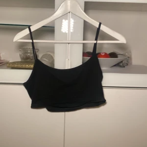 Svart croppad linnetopp - En enkel svart croppad linnetopp med smala axelband. Perfekt att styla till jeans eller kjol för en avslappnad look.