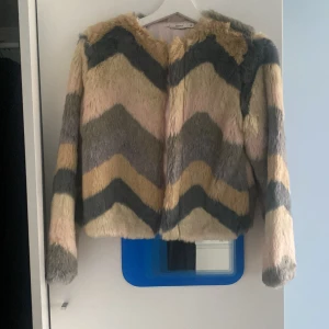 Färgglad pälsjacka från Name It - Säljer en fluffig pälsjacka från Name It i storlek 152. Jackan har coolt sicksackmönster i beige, grått, rosa och gult. Den är långärmad, har tryckknappar och är fodrad med ljusrosa tyg. Perfekt för dig som vill sticka ut med en unik look!