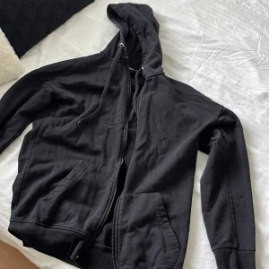 Svart hoodie med dragkedja från Boohoo - Svart hoodie från Boohoo med dragkedja framtill, huva med snörning och två stora fickor. Klassisk modell i mjuk bomullsmix, perfekt för chill dagar. Långärmad och enkel att matcha med allt.