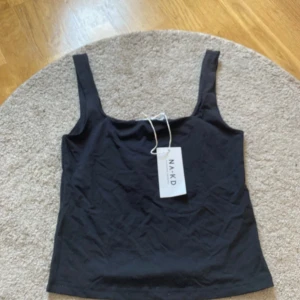 Svart linnetopp från NA-KD - Säljer en svart linnetopp från NA-KD med breda axelband. Enkel och stilren design som passar perfekt till sommaren. Toppen är i mjukt material . Perfekt att matcha med jeans eller kjol!