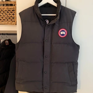 Grå Canada Goose Vest - Tömmer nu garderoben och säljer denna vest eftersom att den inte kommer till användning • Storlek Medium • Grå • Skick= 6.5-7/10 (finns täcken på användning men inga skador eller trådar)   Loggor och detaljer kan gemföras med ann annan javka som är köpt på NK, ifall du undrar om den är äkta! 🙌