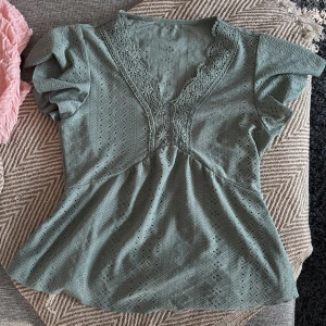 Grön blus med spets och v-ringning - Storlek 38 ( när jag skriver 36/38) beror det på strech eller bröstplats jag har 85 C/D och får inte plats) men passar i övrigt. Supersöt ljusgrön blus med v-ringning och spetsdetaljer längs halsen. Blusen har korta puffärmar och ett broderat hålmönster över hela tyget. Den har en lätt utställd passform och känns både romantisk och trendig.