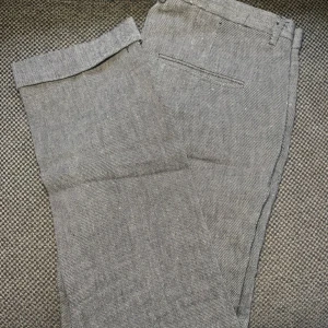 Grå kostymbyxor från H&M, stl 54 - Snygga grå kostymbyxor från H&M i storlek 54. Byxorna har diskret fiskbensmönster, raka ben och klassiska passpoalfickor bak. Perfekta för en clean och stilren look. Materialet känns som en blandning av bomull och polyester.