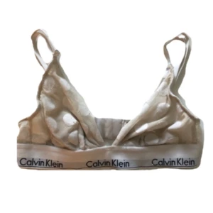 Beige prickig linnetopp Calvin Klein - Snygg beige linnetopp från Calvin Klein med vita prickar och klassiskt logoband under bysten. Topp med smala axelband och mjuk passform, perfekt för en chill och sportig look.