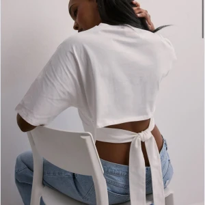 Vit croppad topp med knytband - Säljer en vit croppad topp med korta ärmar och snygga knytband i ryggen. Toppen har en enkel och stilren design med rund halsringning och är perfekt till jeans eller kjol.