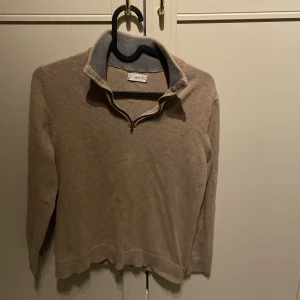 Beige halvzip tröja från Mango - Beige långärmad tröja från Mango med halv dragkedja och hög krage. Tröjan är i mjukt material och har en enkel, clean look som passar perfekt till jeans eller kjol. Ribbad kant vid kragen ger en snygg detalj.