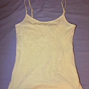 Ljusgul linnetopp från Amisu - Supersöt ljusgul linnetopp från Amisu med smala, justerbara axelband. Enkel och stilren design i mjukt material, perfekt till sommaren. Toppen är ärmlös och har en rak passform som funkar till många olika looks.