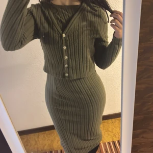 Olivgrön ribbad långklänning - Säljer en olivgrön ribbad långklänning med lång ärm och v-ringning. Klänningen har en figurnära passform och dekorativa knappar framtill. Materialet är stickat och mjukt, perfekt för dig som gillar en stilren och bekväm look.