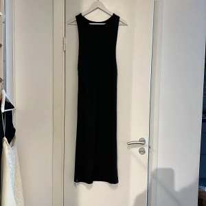 Strandklänning med knytdetalj - Säljer en svart strandklänning med ärmlös design och knytdetalj i midjan. Klänningen har en stilren och rak passform, tillverkad i ett ribbat material som ger en snygg struktur. 