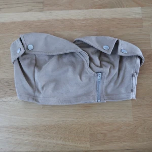 Beige tubtopp med dragkedja och knappar - Säljer en beige tubtopp med dekorativa knappar upptill och dragkedja framtill. Som ny, bara använd några få gånger, normal i storleken