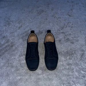 Christian Louboutin - Säljer ett par mörkblå sneakers från Christian Louboutin med klassisk röd sula och snörning. Skorna är i mocka och har rund tå. Perfekta för dig som gillar lyxiga detaljer och stilren design.