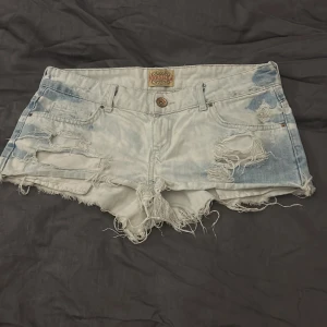 Ljusblå slitna jeansshorts från Bershka - Säljer ett par ljusblå jeansshorts från Bershka med slitna detaljer och fransig kant. Shortsen har klassisk femficksdesign, låg midja och knappgylf. Perfekta för sommardagar och festivaler. Priset kan diskuteras😊