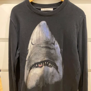 Svart sweatshirt med hajmotiv från Givenchy - Säljer denna tröja från Givenchy då den inte kommer till användning. Den är i bra skick och är i storlek S. Dock ett litet hål på ryggen men inget som syns 