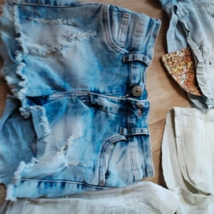 Ljusblå jeansshorts med slitningar - Säljer ett par ljusblå jeansshorts med fransig kant och slitna detaljer. Klassisk femficksmodell med knapp och dragkedja. Perfekta för sommaren och ger en cool, avslappnad look.