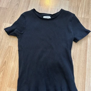 Svart ribbad t-shirt från Lindex - En svart ribbad t-shirt från Lindex med rund halsringning och korta ärmar. Enkel och stilren modell som passar till det mesta. Mjuk och stretchig känsla tack vare ribbat material. Storlek S