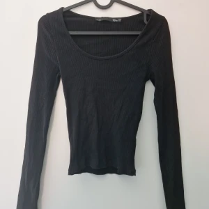 Svart ribbad långärmad topp från Lager 157 - Säljer en svart, ribbad långärmad topp från Lager 157. Modellen är tight med rundad, djup ringning och smal passform. Perfekt att styla med jeans eller kjol. Materialet är stretchigt och bekvämt.