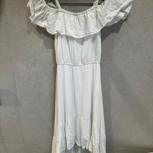 Vit långklänning med volang - Superfin vit långklänning med bred volang upptill och axelband. Klänningen har en romantisk känsla och är perfekt för sommarens alla tillfällen. Lätt och luftig modell med offshoulder-look.