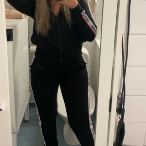 Svart sett från Moschino - Svart sett från Moschino med dragkedja och vita logoband längs ärmarna, samt vit logoband längs benen. Sportig look med normal passform. Perfekt för dig som gillar att sticka ut med en snygg logga. L i byxan S i tröjan, små i storleken. Använd 1 gång. Äkta