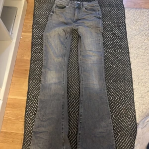 Grå bootcut jeans från ONLY - Säljer ett par grå bootcut jeans från ONLY med klassisk femficksdesign och knappgylf. Jeansen har breda benslut och markerade sömmar, perfekt för dig som gillar en retroinspirerad look. Använt 1 gång:))