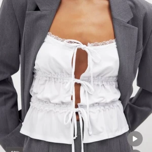 Vit linnetopp med spets och knyt - Söt vit linnetopp med smala axelband, spetsdetaljer och tre knyt framtill. Ny, prislapp kvar .