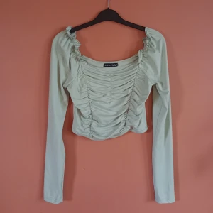 Ljusgrön långärmad topp - Ljusgrön långärmad topp med rynkor framtill och volangdetaljer vid axlarna. Toppen har en fyrkantig urringning. Köpt på Sellpy men ursprungligen från Shein, fint skick och endast använd 1 gång. Mycket stretchig i tyget 💚 Storlek S