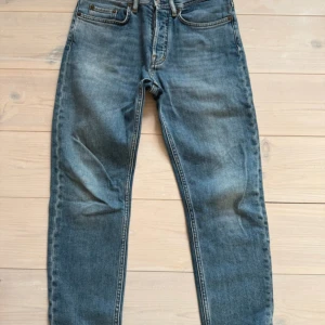 Acne Studios Jeans - Säljer ett par klassiska blå jeans från Acne Studios med fem fickor och raka ben. Jeansen har normal passform och är tillverkade i denim med snygga slitningar framtill. Perfekta för en stilren och avslappnad look.