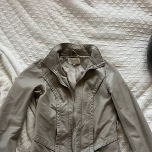Grå skinnjacka - Säljer en beige/grå jacka från Vila med snyggt figursydd passform och dragkedja framtill. Perfekt för vår och höst, Köpt second hand och knappt använd av mig. Har lite slitningar i kragen men inget som syns när man har den på sig (se bild)