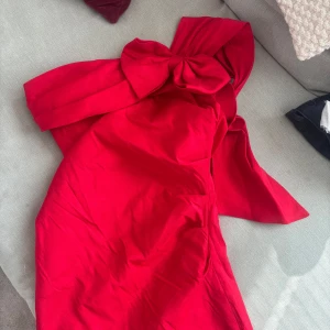 Röd one shoulder-klänning med stor rosett från LENA - Säljer en röd one shoulder-klänning från LENA med en stor dekorativ rosett vid axeln. Klänningen har en figurnära passform och är tillverkad i polyester. Jag bär vanligtvis storlek S/M och denna är aningen tajt. Tveka inte på att höra av dig vid frågor eller prisförslag!