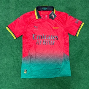 AC Milan röd och grön fotbollströja från Puma - Säljer en officiell AC Milan fotbollströja från Puma med röd överdel och grön nedre del i snygg fade. Tröjan har svarta och gula detaljer på krage och ärmslut samt tryck med 'Emirates Fly Better' och 'DIAVOLI' på bröstet.
