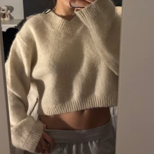 Beige croppad stickad tröja med v-ringning - Mysig beige croppad stickad tröja med v-ringad hals och långa ärmar. Perfekt för lager-på-lager och ger en avslappnad men trendig look.