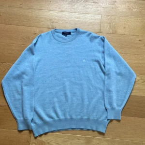 Ljusblå stickad tröja från Burberry - Stilren och klassisk tröja i blåmelerat tyg med diskret broderad logga framtill. Storlek M, men passar bättre som S–M beroende på hur du vill att den ska sitta. Perfekt basplagg med lyxig känsla – mjuk, bekväm och lätt att matcha. Skick: Väldigt bra. Priset är självklart förhandlingsbart vid snabb affär – hör av dig!
