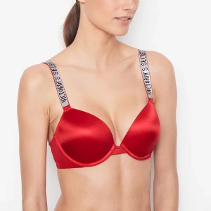 Röd push-up bh Victorias secret - Snygg röd push-up bh med glansig finish och breda axelband med logotyp-tryck. Bh:n har bygel och vadderade kupor för extra lyft och stöd. Perfekt för dig som vill ha en statement-bh med sportig känsla. Aldrig använd.