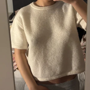 Vit stickad croppad tröja - Säljer en vit stickad tröja med korta ärmar och croppad passform. Tröjan har en rund halsringning och är perfekt för en avslappnad och trendig look. Supermjuk och enkel att matcha med olika outfits.