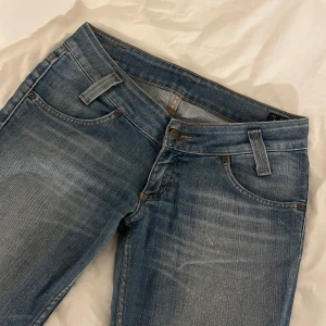 Blå bootcut jeans från Lee - Säljer ett par klassiska blå bootcut jeans från Lee med fem fickor och dragkedja. Jeansen har en lätt tvättad look och normal passform. Perfekta för dig som gillar en tidlös stil.