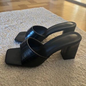 Svarta klackade sandaler  - Säljer ett par svarta sandaler med bred rem och fyrkantig tå. Skorna har hög blockklack och en stilren look. Använda en gång, säljer då de är aningen trånga då jag normalt har storlek 39. Inget slitage. Från H&M