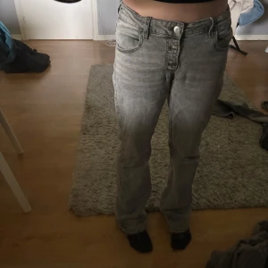 Grå bootcut jeans med knappar - Säljer ett par grå jeans med bootcut passform och låg midja. Byxorna har 3 knappar framtill och klassiska fickor både fram och bak. Dom är lite uttöjda så de sitter lite löst och tror det skulle passa lite större storlek också.