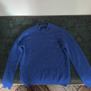 Blå stickad tröja från Massimo Dutti - Säljer en klassisk blå stickad tröja från Massimo Dutti. Tröjan har rund halsringning, långa ärmar och ribbade muddar vid ärmslut och nederkant. Perfekt för lager-på-lager under kyliga dagar.