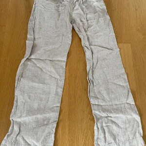 Beiga linnebyxor från Gina Tricot - Snygga och luftiga beiga linnebyxor från Gina Tricot. Byxorna har raka ben och normal passform, perfekta för varma dagar. Tillverkade i ett mjukt linnematerial som ger en avslappnad och stilren look.