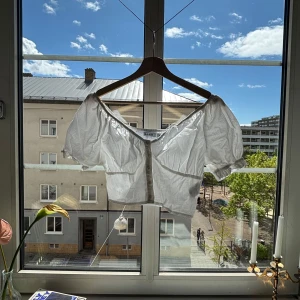 Vit croppad blus från NA-KD - Superfin vit croppad blus från NA-KD med puffiga korta ärmar och knappar framtill. Offshoulder-modell med resår vid axlarna för en snygg passform. Perfekt till jeans eller kjol för en trendig look. Aldrig använd, enbart testad! 