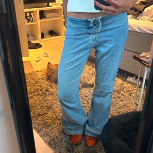 Ljusblå jeansbyxor med snörning - Säljer ett par ljusblå jeansbyxor med snygg snörning framtill i midjan. Byxorna har låg midja och en rak, något utsvängd passform. Perfekta för dig som gillar en avslappnad och trendig stil. Passar från 34-38 skulle jag säga! Ge prisförslag💕