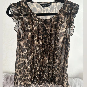 Leopardmönstrad blus med volang  - Säljer en transparent blus med leopardmönster. Blusen har volangdetaljer framtill och vid ärmarna samt är ärmlös. Aldrig använd! 