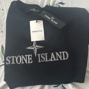 Svart sweatshirt från Stone Island - Säljer en svart sweatshirt från Stone Island med stor broderad logga på bröstet och klassisk patch på ärmen. Tröjan har rund halsringning och normal passform. Perfekt för dig som gillar streetwear och vill ha något stilrent. Men kan bara mötas upp