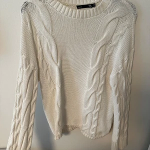 Vit stickad tröja med flätmönster  - Säljer en vit stickad tröja från lager 157 med grovt flätmönster på både fram- och baksida samt ärmar. Tröjan har rund halsringning och långa ärmar. Perfekt för kyligare dagar.